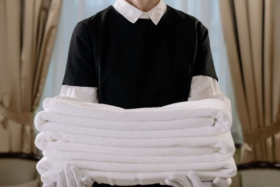 A woman carefully wraps a sofa in protective material while packing boxes in a bright room.
